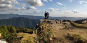 火上げ岩の上に立つ二人と広がる山々のパノラマ